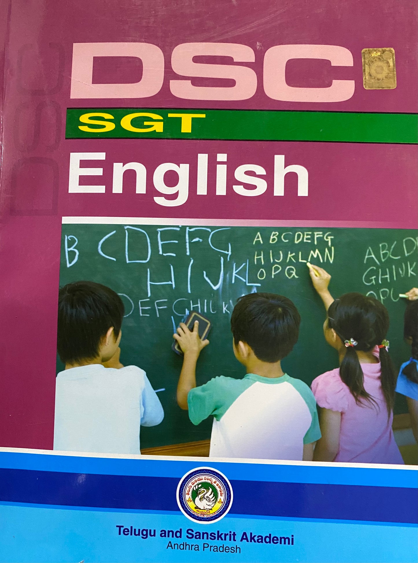 The cover of the "DSC SGT English" textbook by the Telugu and Sanskrit Akademi, showing children writing the alphabet on a chalkboard.